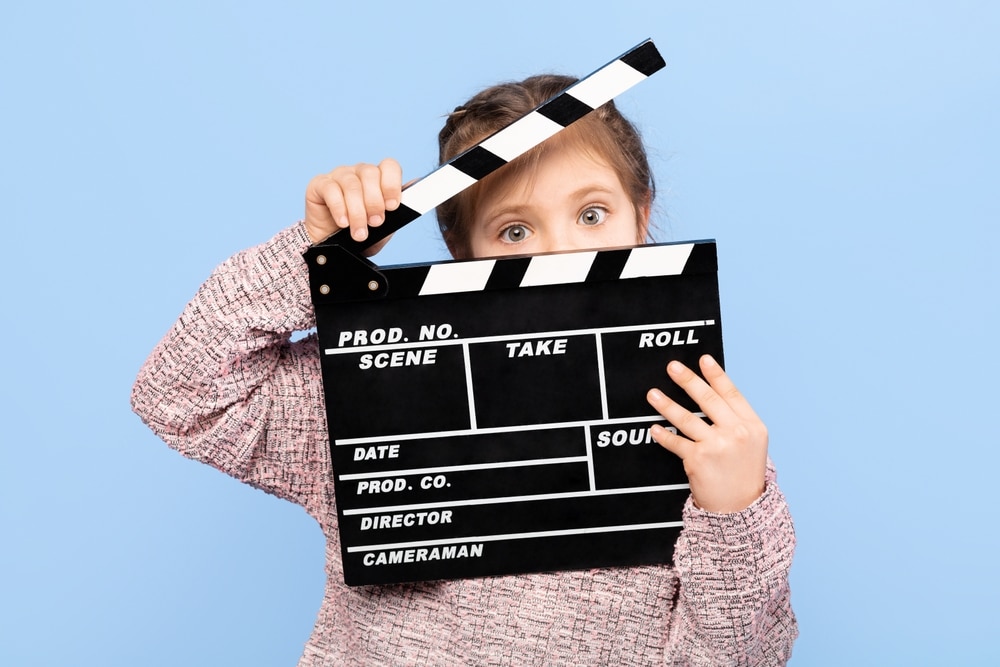 Acheerfulgirlposeswithaclapperboardembodyingcreativityand - Rick's Blog