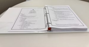 Open three-ring binder with printed documents on a white round table, view from above in an office setting.