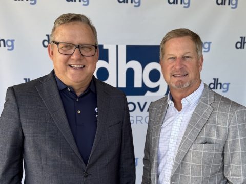 Two smiling men in business attire pose together in front of a dhg banner.