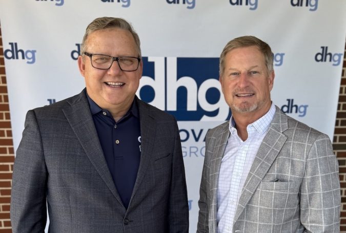 Two smiling men in business attire pose together in front of a dhg banner.