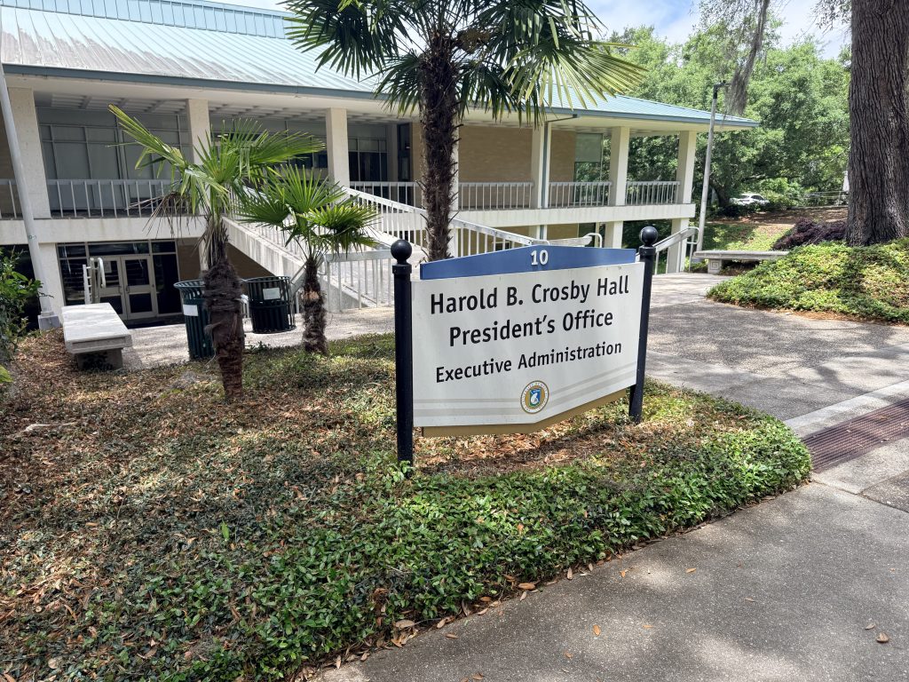 Sign for Harold B. Crosby Hall near a walkway with palm trees at a campus building entrance.