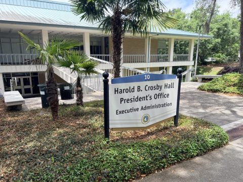 Sign for Harold B. Crosby Hall near a walkway with palm trees at a campus building entrance.