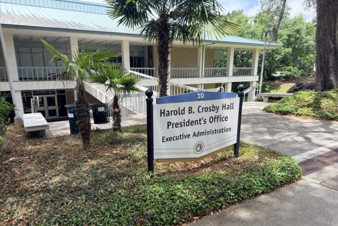Sign for Harold B. Crosby Hall near a walkway with palm trees at a campus building entrance.