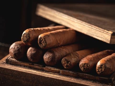 Cigars arranged in a rustic wooden box with the lid resting nearby, and an old book on top.