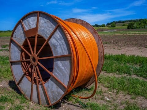 Large orange cable reel (spool) lying on a dirt and grass field under a clear blue sky, outdoors.