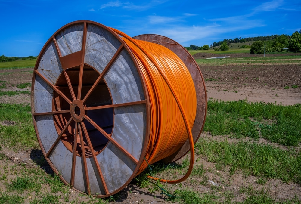 Large orange cable reel (spool) lying on a dirt and grass field under a clear blue sky, outdoors.