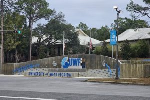 Entrance to University of West Florida with a large UWF logo sign, blue railings, and steps behind.