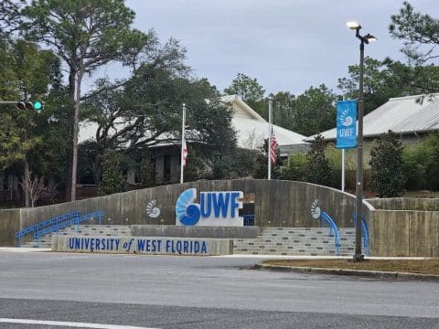 Entrance to University of West Florida with a large UWF logo sign, blue railings, and steps behind.