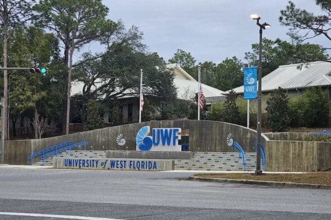 Entrance to University of West Florida with a large UWF logo sign, blue railings, and steps behind.