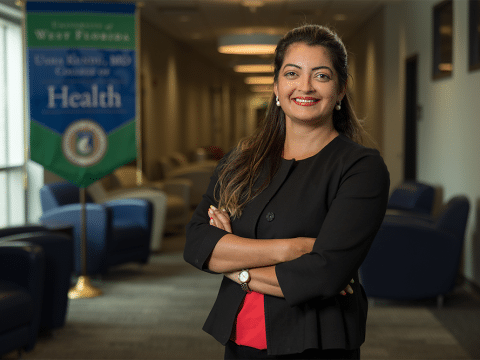 Professional woman with arms crossed in a clinic lobby, visible health banner in the background.