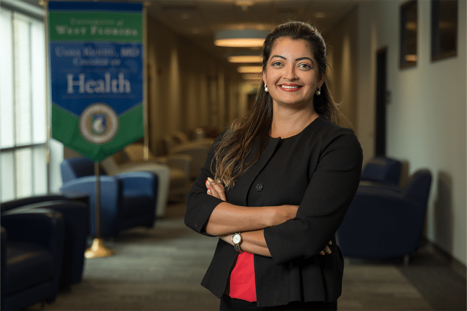 Professional woman with arms crossed in a clinic lobby, visible health banner in the background.