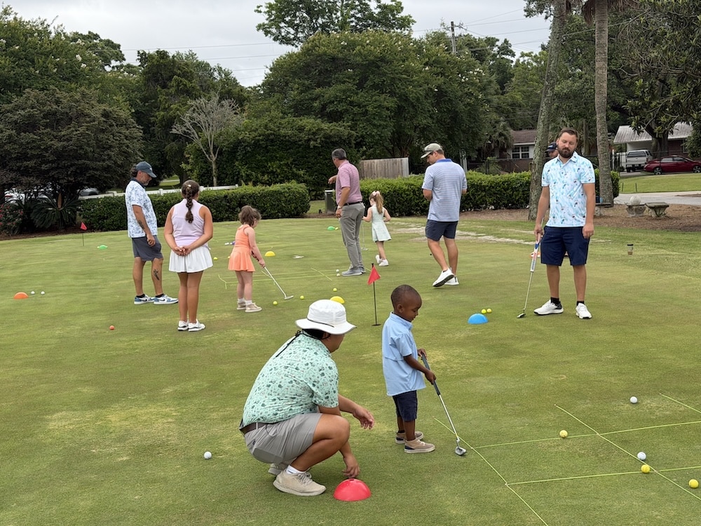 Adults and children practicing golf on a sunny putting green with cones and flags.