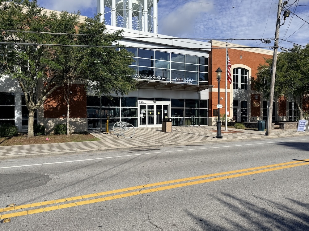 Public civic building with a glass entrance, brick facade, and an American flag outside on a sunny day.