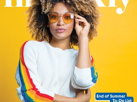 Portrait of a woman with curly hair in a white sweater with rainbow sleeves, yellow background, wearing orange sunglasses, on a magazine cover