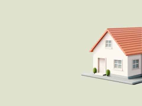 Model white house with a red gabled roof and chimney on a raised platform against a pale beige background