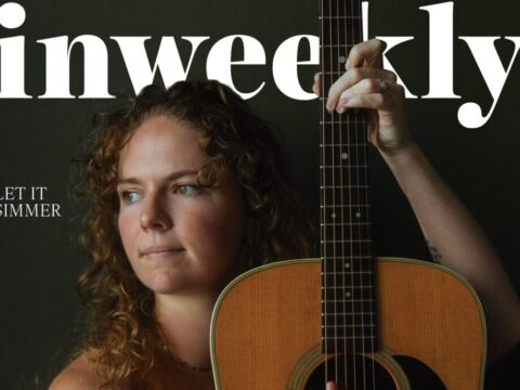 Portrait of a woman with curly hair holding an acoustic guitar, on a magazine cover with large 'weekly' text and 'Katie Dineen' featured