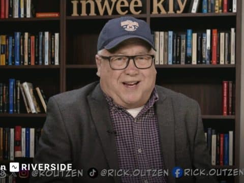 Smiling man in a blazer and cap speaks to the camera in front of a bookshelf backdrop; Riverside branding appears at the bottom left.