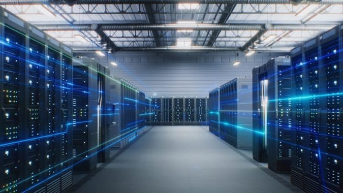Data center with long rows of server racks and blue light streaks suggesting data flow.